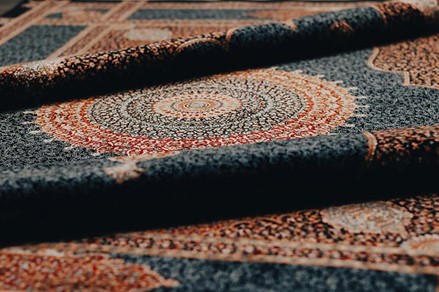 Persian Rug vs Turkish Rug A close-up shot of a rolled carpet with a prominent circular medallion design in shades of red, orange, and cream against a dark background.