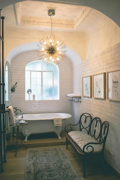 A stunning blend of vintage charm and modern flair. The arched doorway, claw-foot tub, and sputnik chandelier create a truly unique and elegant bathroom. Photo by Luis  Ruiz