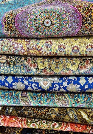 Unveiling the Elegance of a Qum Silk Carpet A close-up shot of a colorful stack of Persian-style rugs, showcasing a variety of intricate patterns and rich colors, including blue, yellow, and purple.